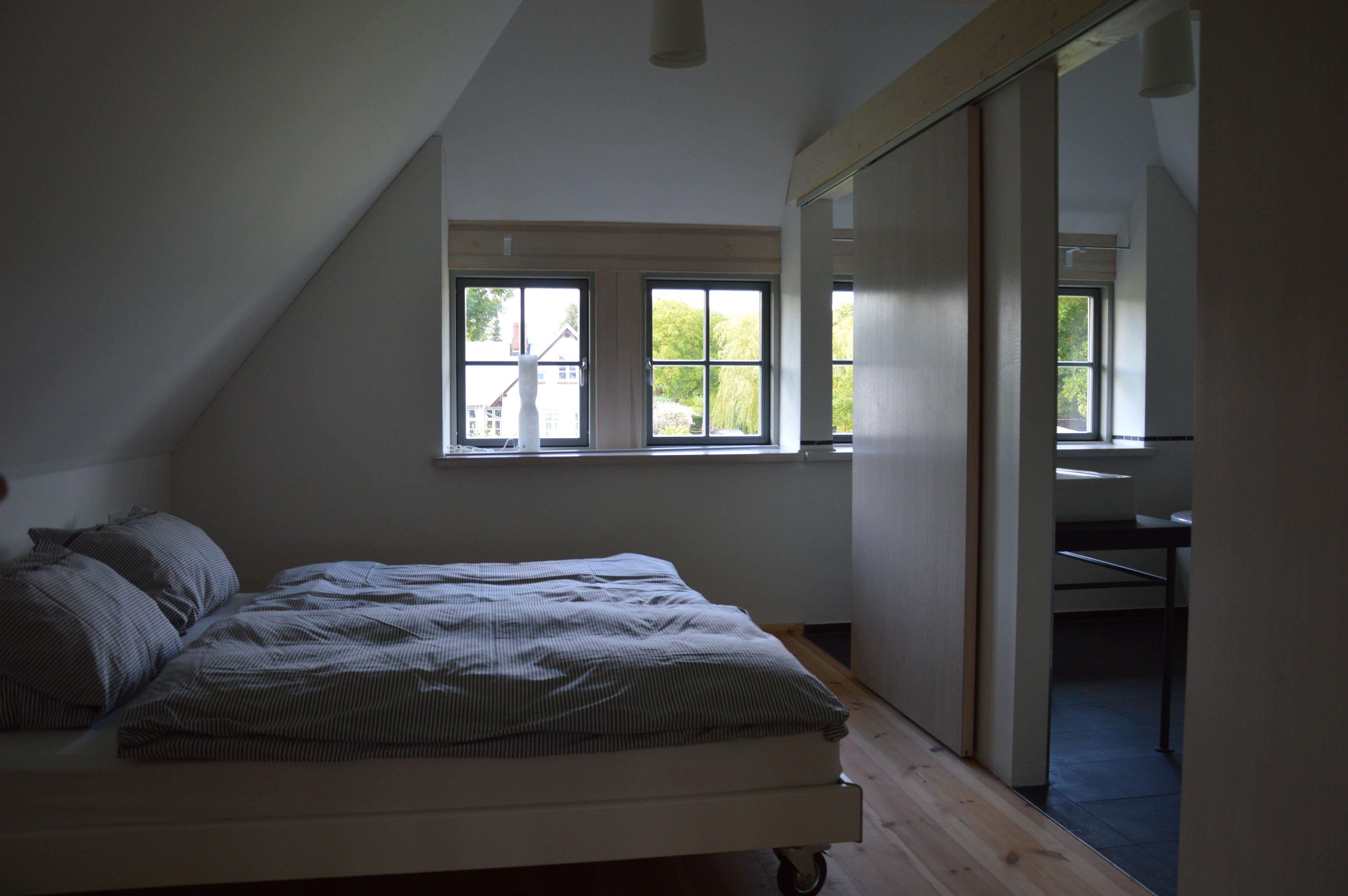 A bedroom with a bed, a window, and a door leading to another room.