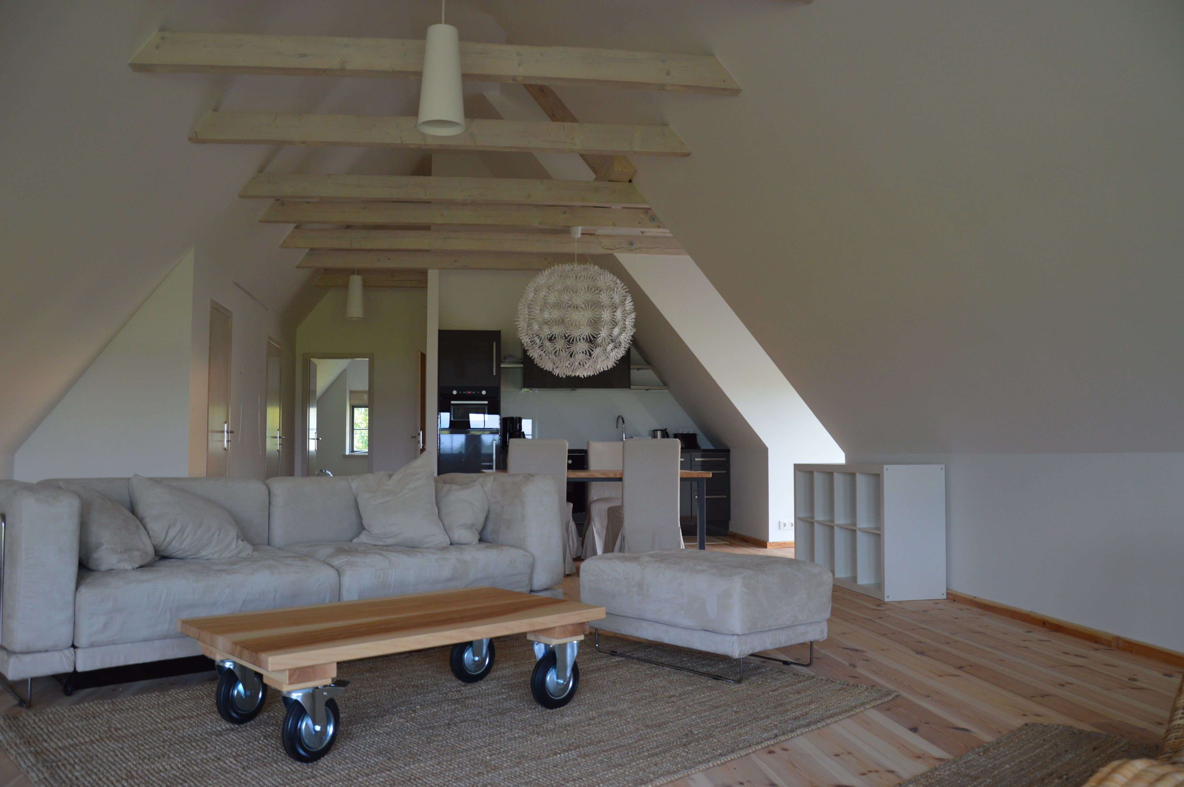 Un loft spacieux avec de hauts plafonds, une cuisine moderne, un coin salon avec un canapé et une table basse, et un coin repas agrémenté d’un lustre.