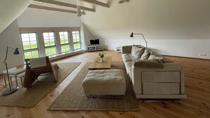 Een ruime loft met hoge plafonds, grote ramen, een moderne bank, een salontafel en een televisie.