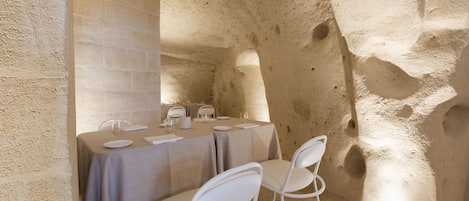 Un comedor con una mesa dispuesta para cuatro, sillas blancas y una pared de piedra.