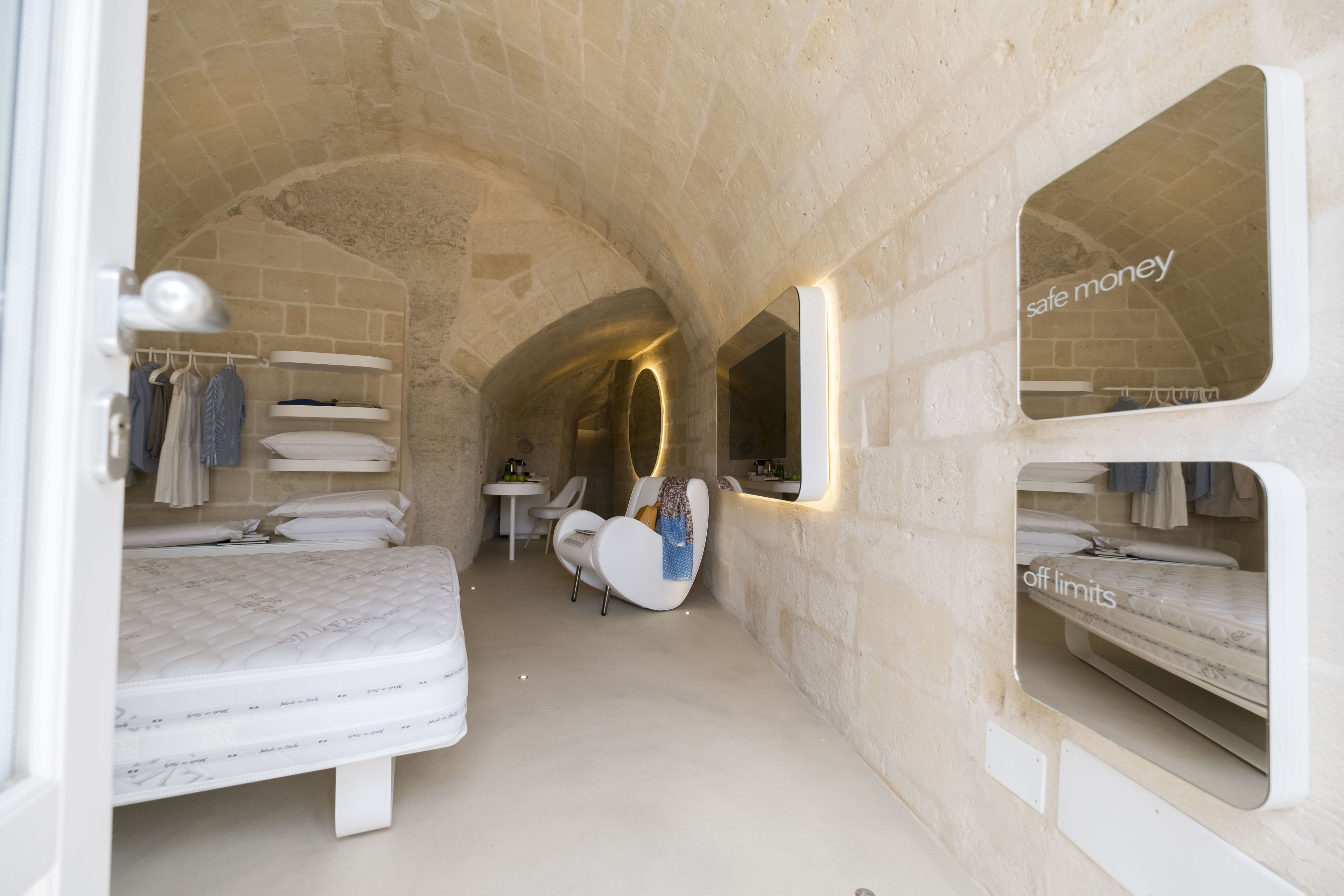 Una stanza stretta ad arco con un letto, una sedia e un tavolino.