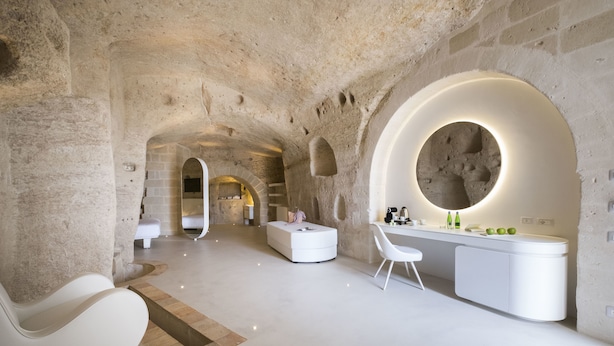 A modern interior with a stone wall, a round mirror, a white sofa, and a white desk with a chair.