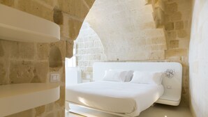 A modern bedroom with a stone wall, a white bed, and a built-in shelf.