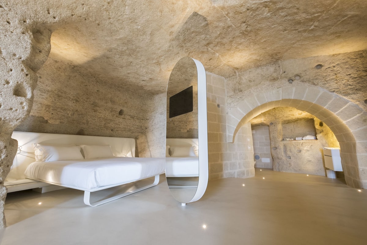 A modern bedroom with a white bed, a stone wall, and a built-in fireplace.