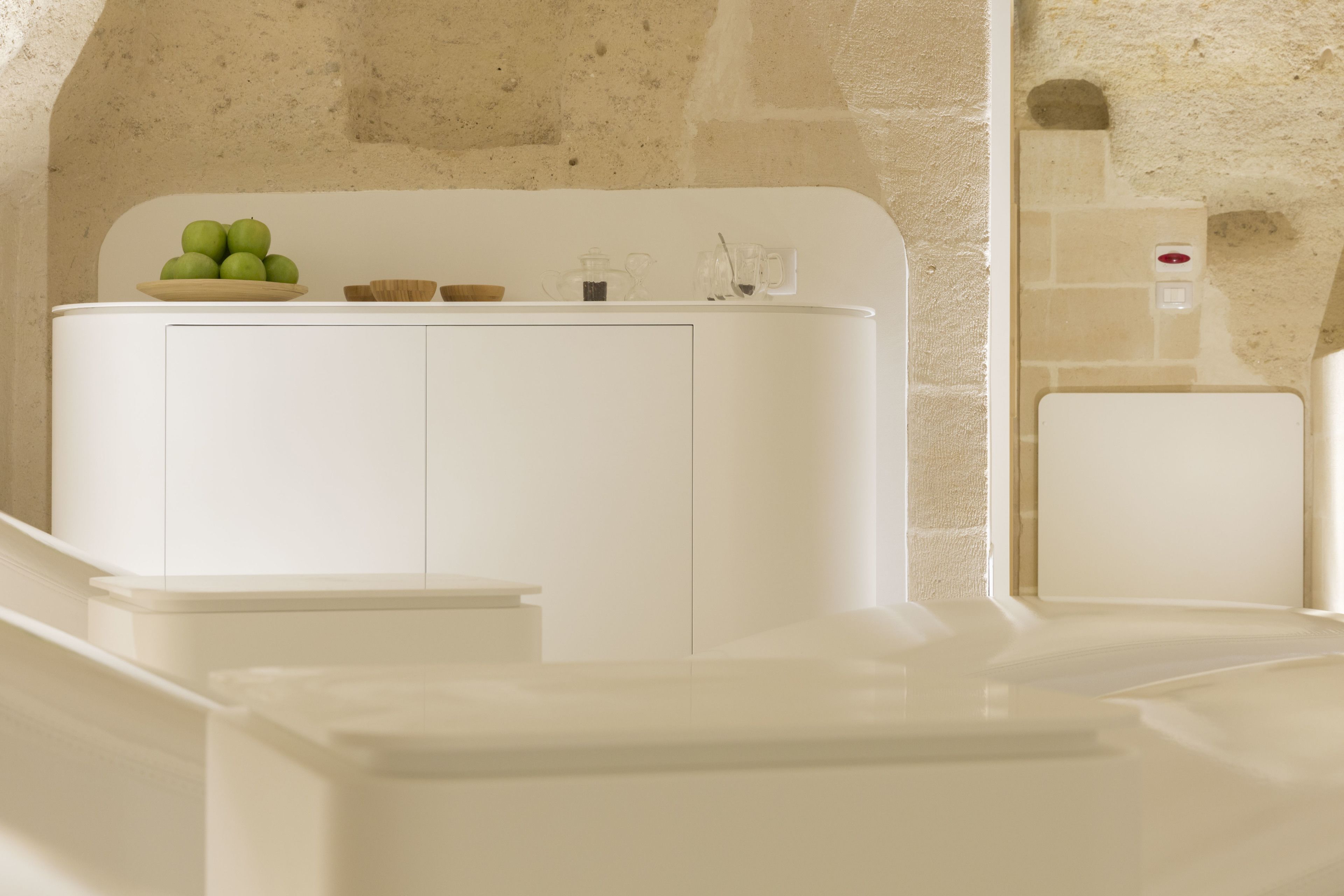 A white bathroom with a sink, a bowl of green apples, and a mirror.