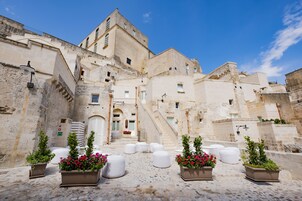Un edificio histórico de piedra con una escalera central, plantas en macetas y un patio empedrado.