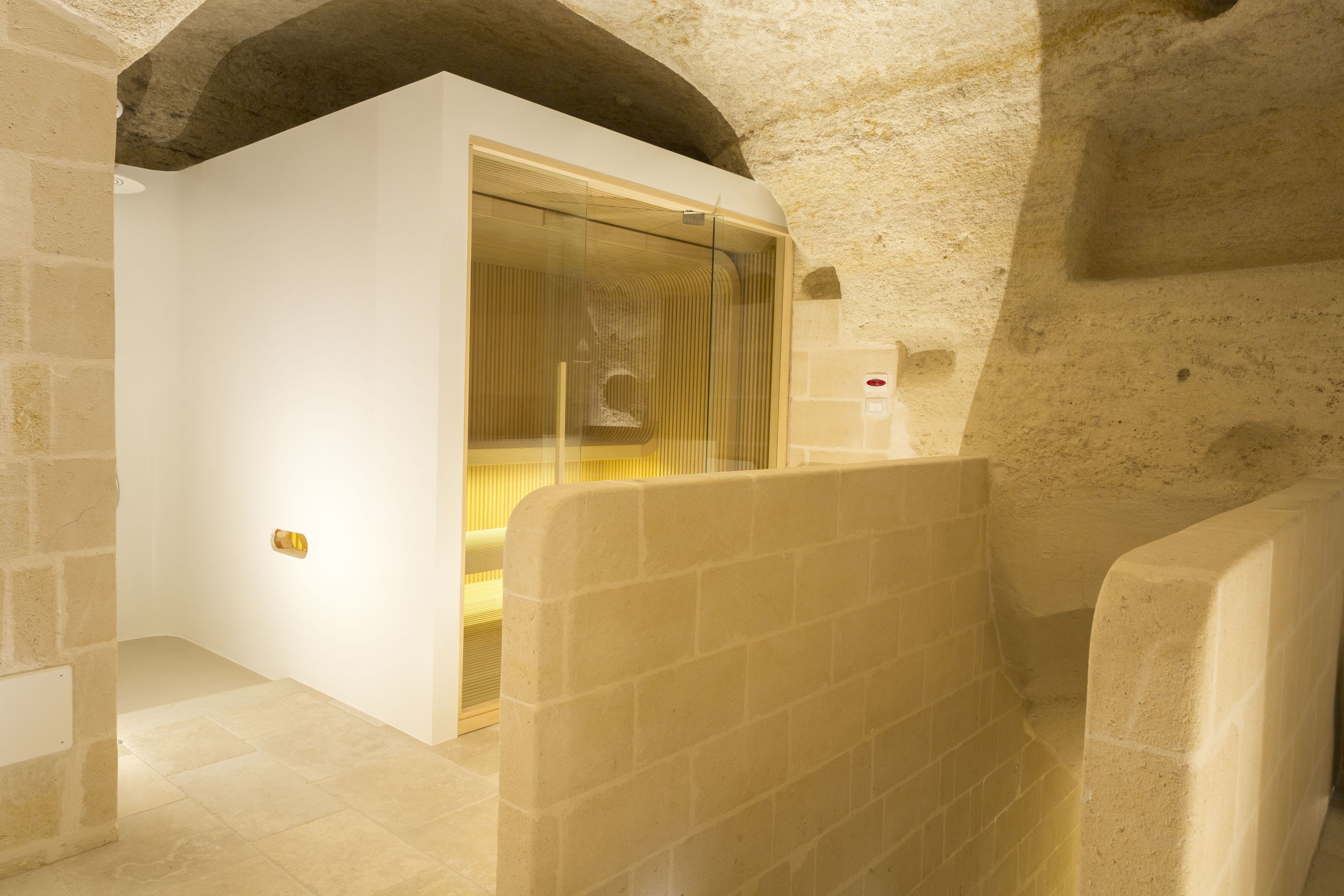 A bathroom with a glass shower enclosure, a towel rack, and a stone wall.