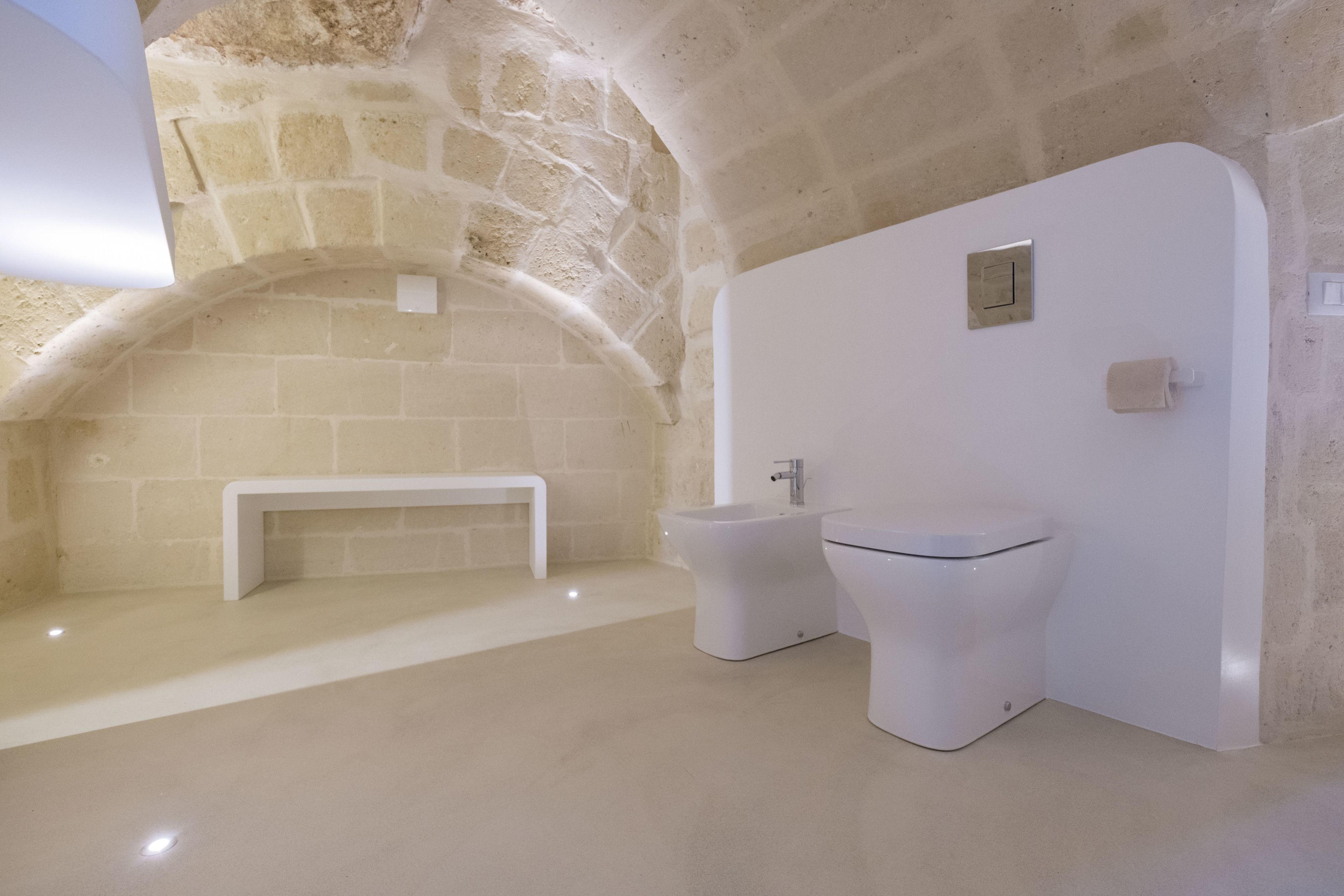 A bathroom with a stone arch, a bench, and a modern toilet.