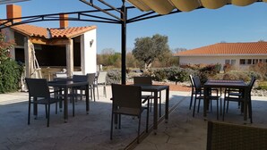 Un patio al aire libre con mesas y sillas, un área de estar techada y vista a una casa con techo de tejas.