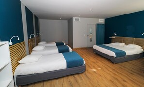 Habitación de hotel con tres camas, suelo de madera y diseño moderno.