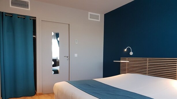 Habitación de hotel con una cama grande, una cortina azul, una puerta con espejo y un aplique de pared.