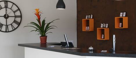 A modern reception desk with a clock, potted plant, and orange storage boxes.