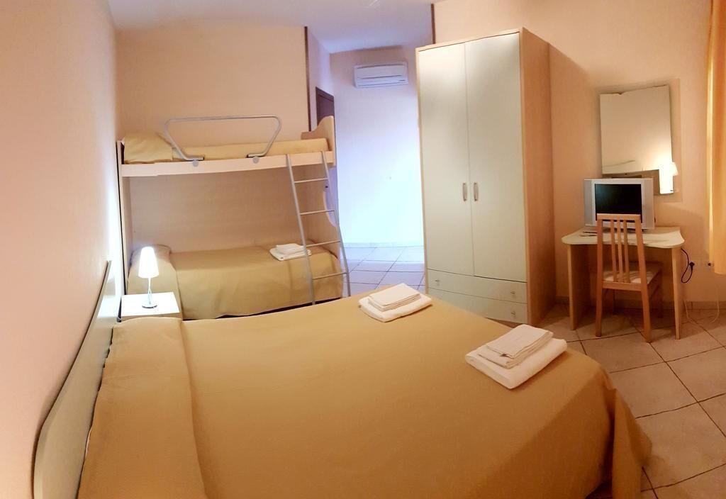 A room with bunk beds, a desk, a chair, a wardrobe, and a lamp.