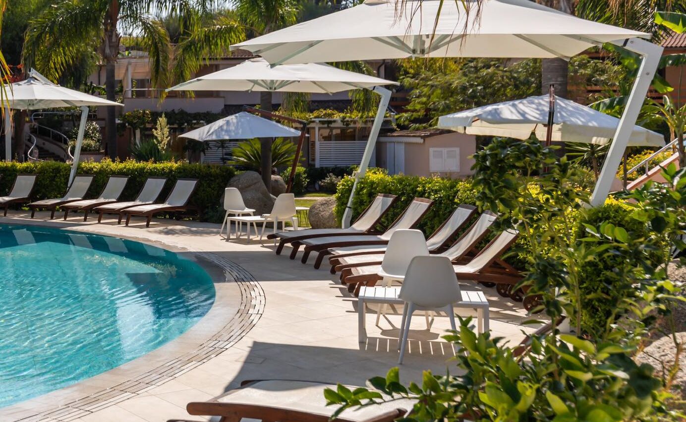 A poolside area with lounge chairs and umbrellas, surrounded by greenery.