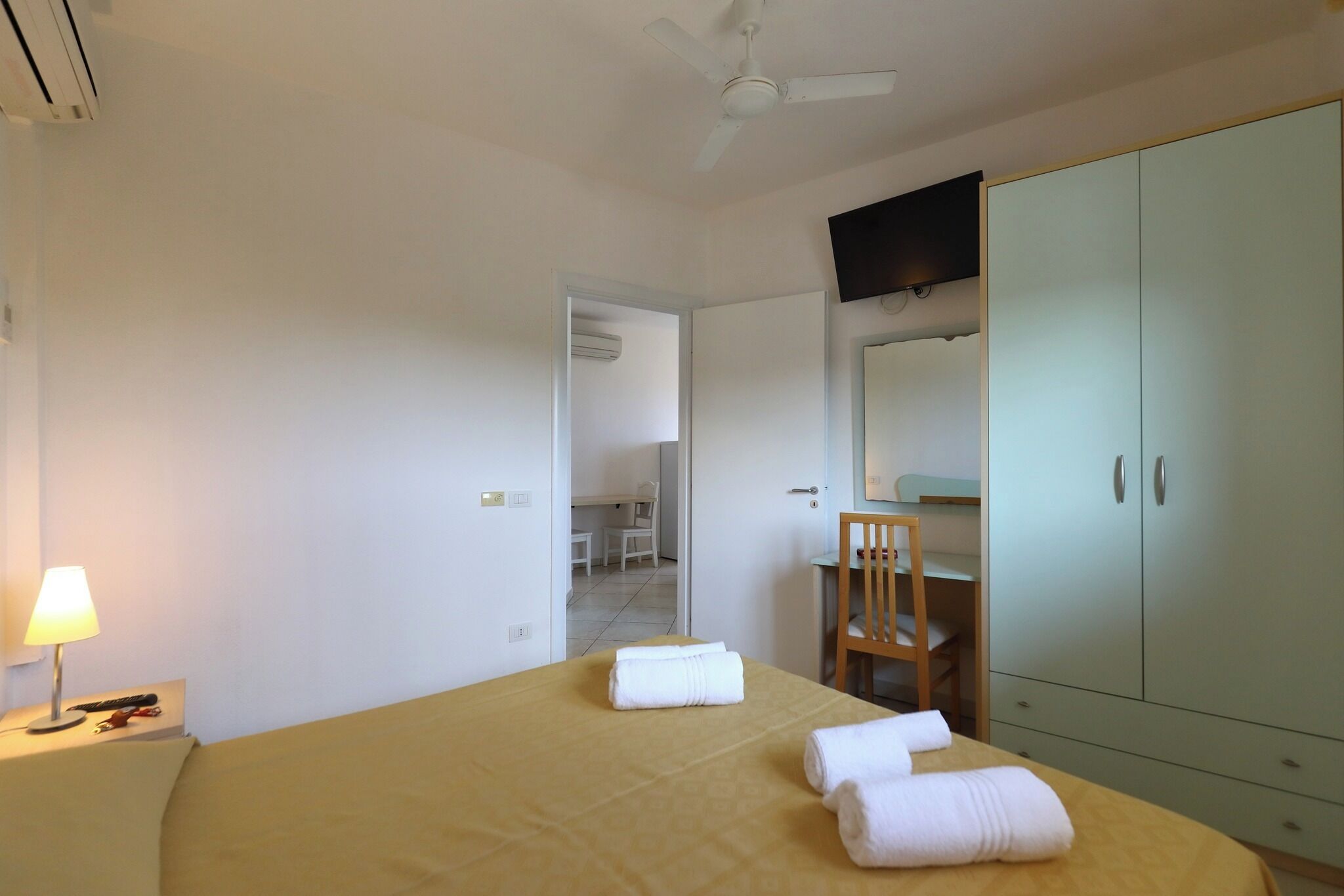 Een hotelkamer met een bed, bureau, stoel, kledingkast en plafondventilator.