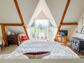 Un dormitorio con una cama grande, televisor, chimenea y un balcón con mesa y sillas.