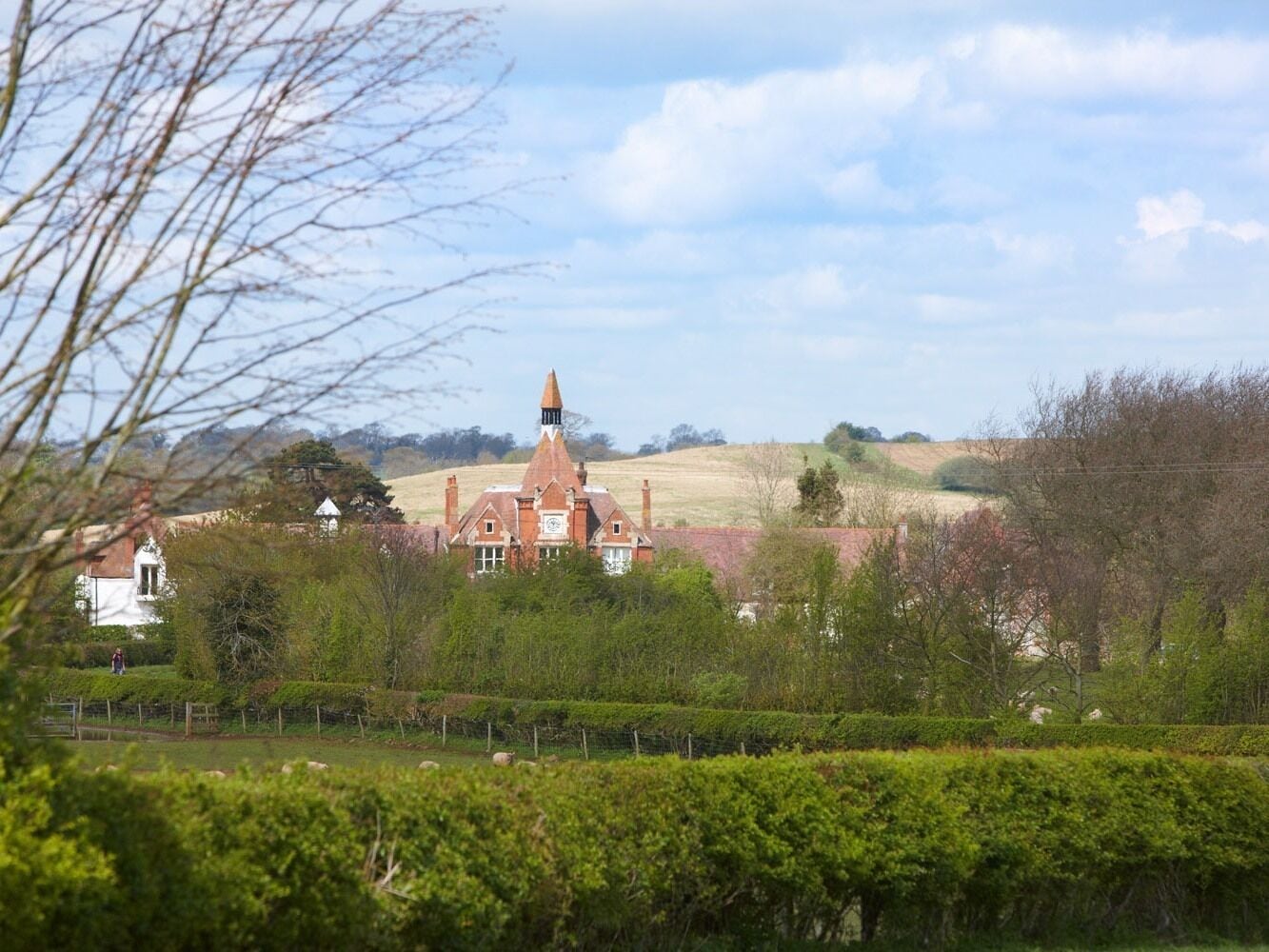 A large, historic building with a prominent tower, surrounded by lush greenery and rolling hills.