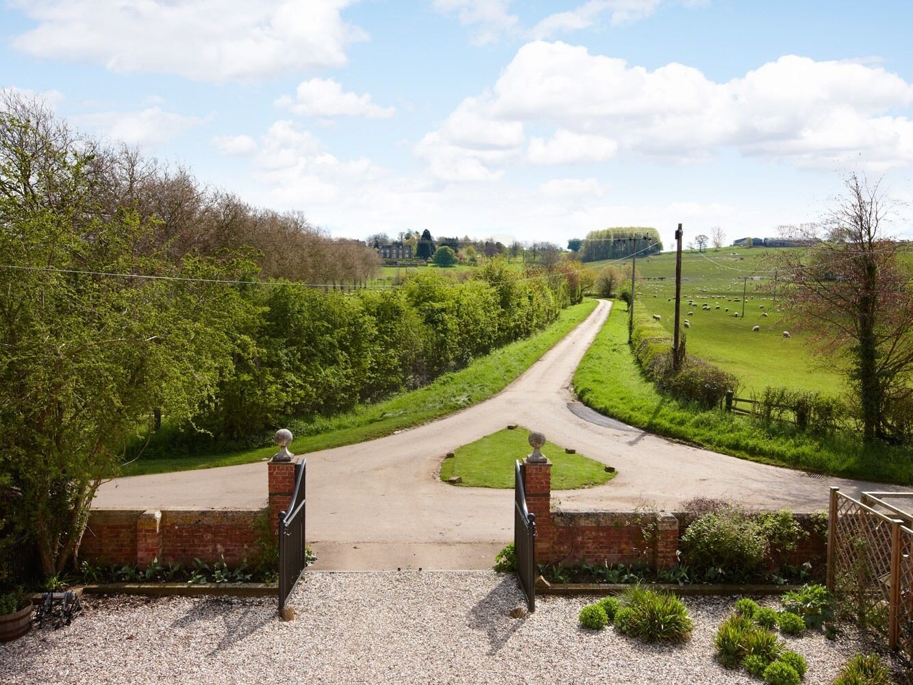A rural landscape with a gravel driveway leading to a gated entrance.