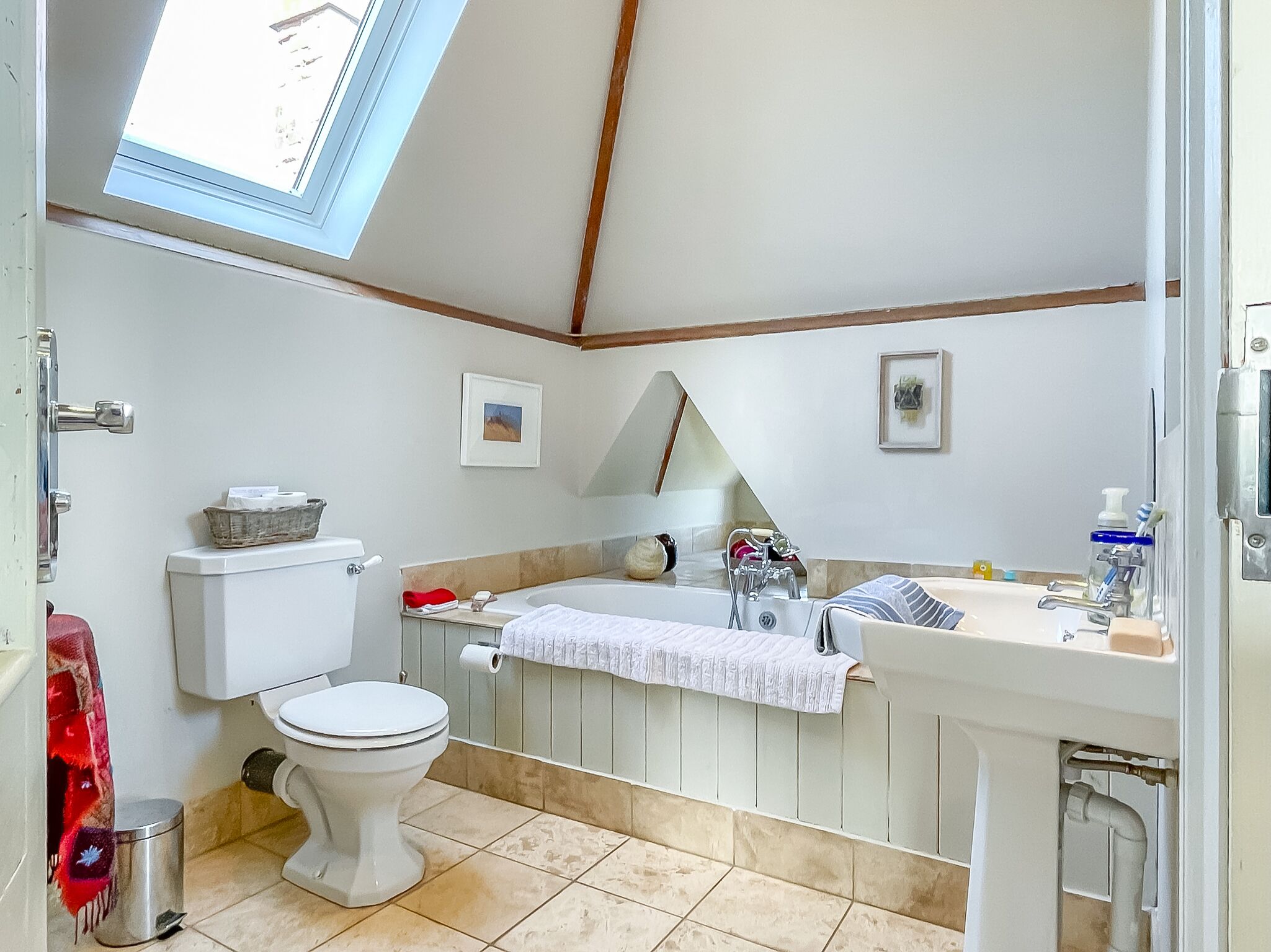 A bathroom with a skylight, toilet, bathtub, and sink.