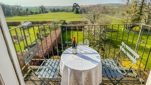 Un balcón con una mesa lista para dos personas, con vista a un paisaje verde.