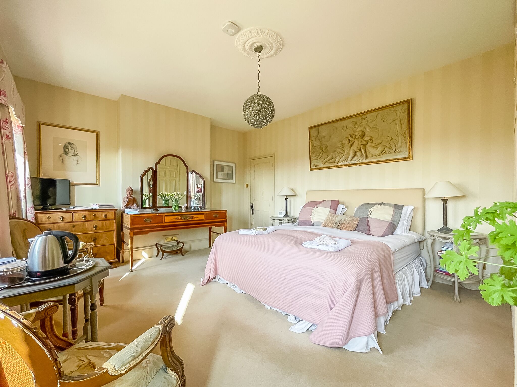 A bedroom with a bed, a desk, a chair, a dresser, a television, and a ceiling light.
