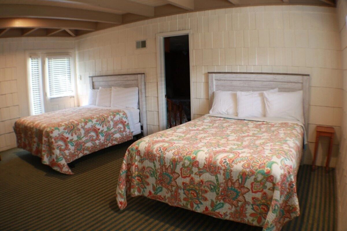 Dos camas individuales con cubrecamas florales en una habitación con paredes de ladrillo blanco y techo inclinado.