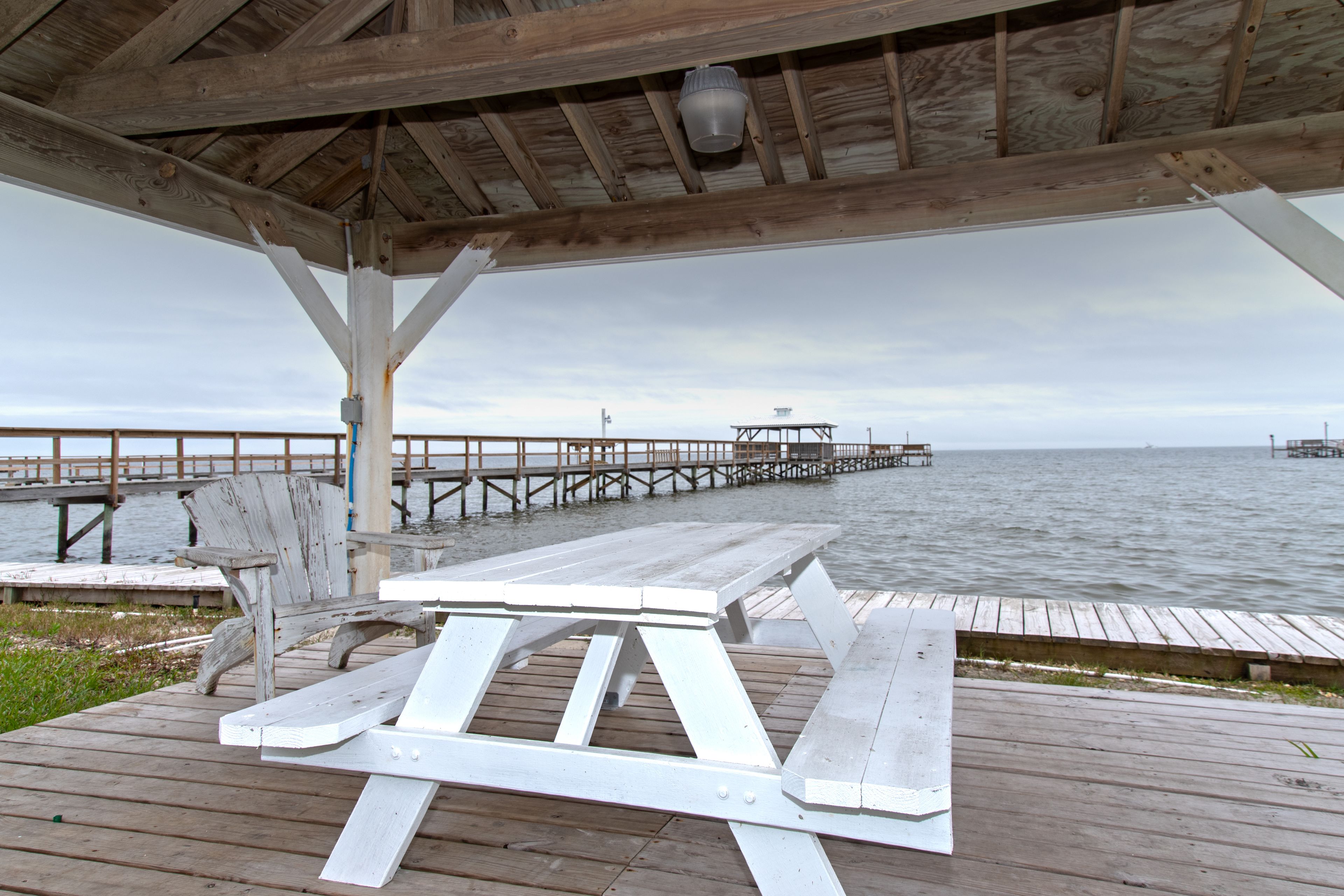 A wooden pier extending into a body of water with a covered seating area and a view of the distant shoreline.