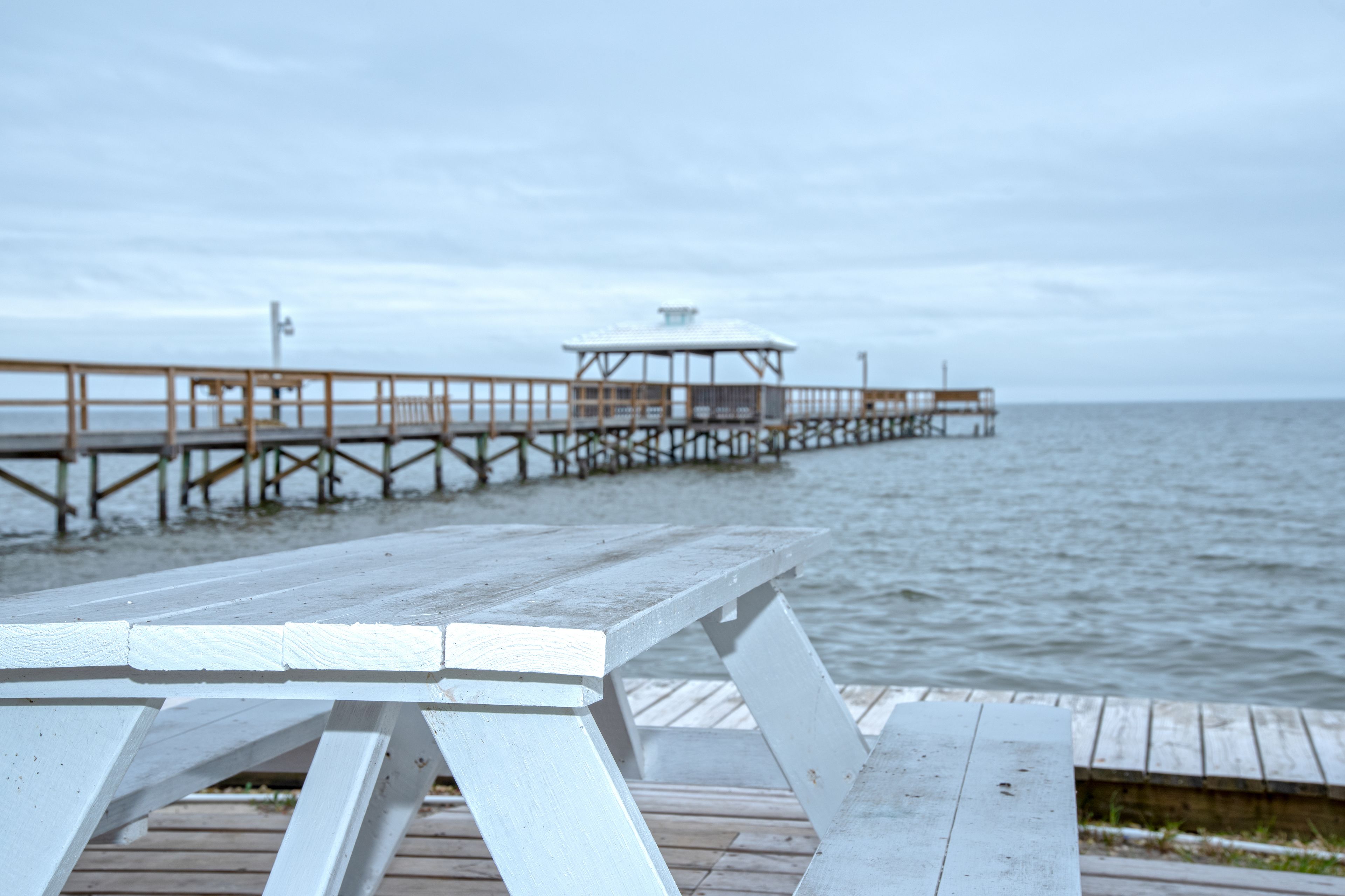 A wooden pier extending into the water with a white picnic table in the foreground.