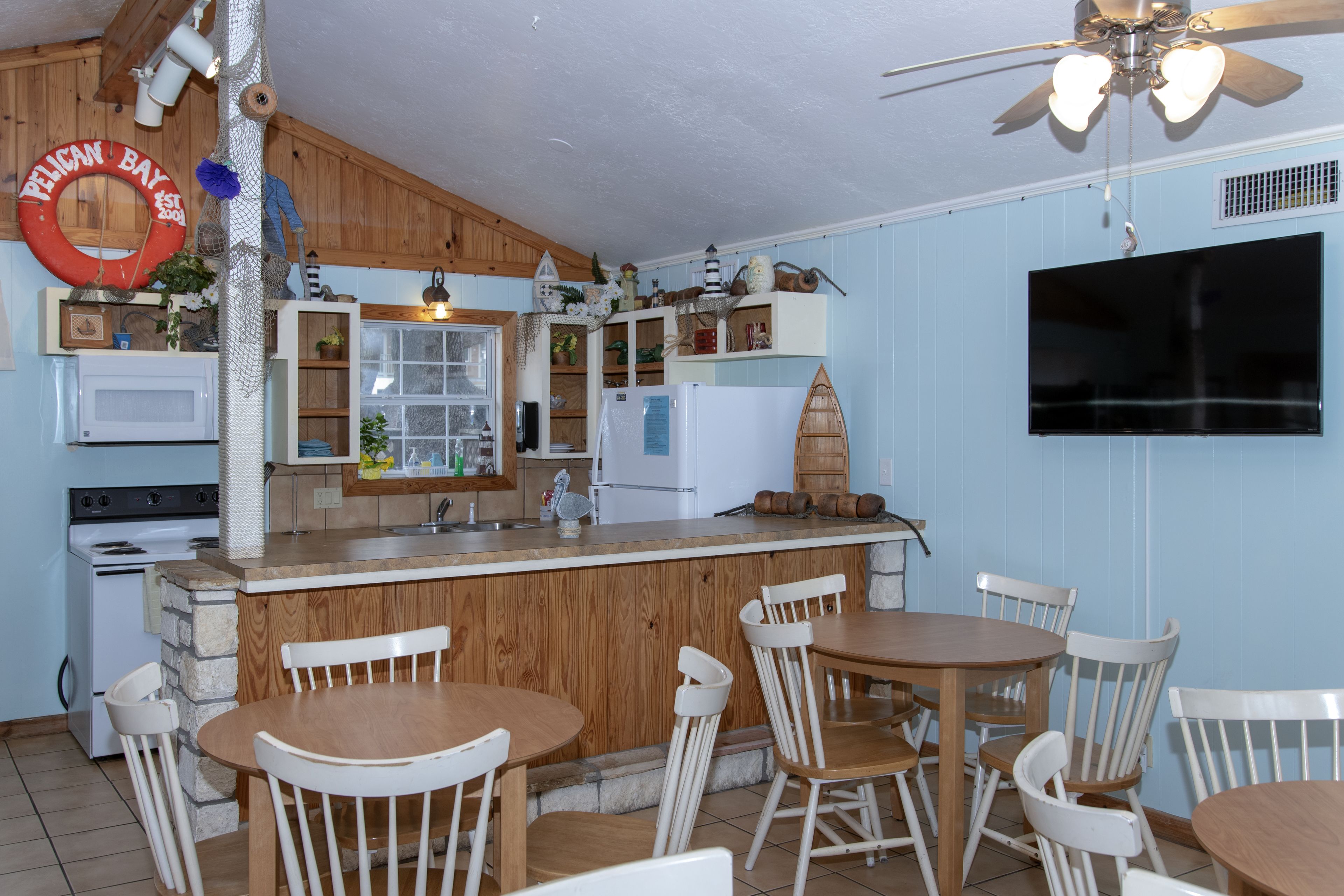 Une cuisine compacte avec des meubles en bois, un réfrigérateur blanc, un four à micro-ondes et un coin repas comprenant des chaises blanches et une table en bois.