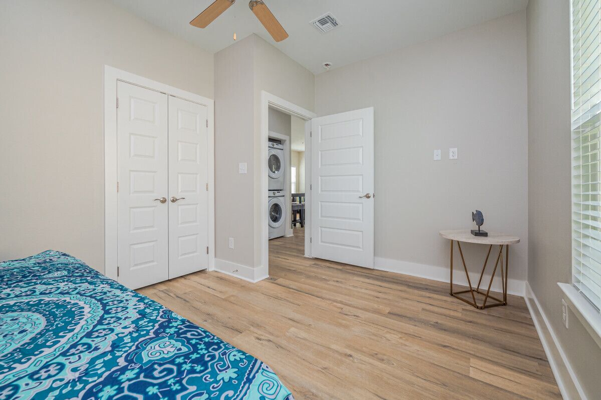 A bedroom with a bed, a ceiling fan, and a view into the laundry room.