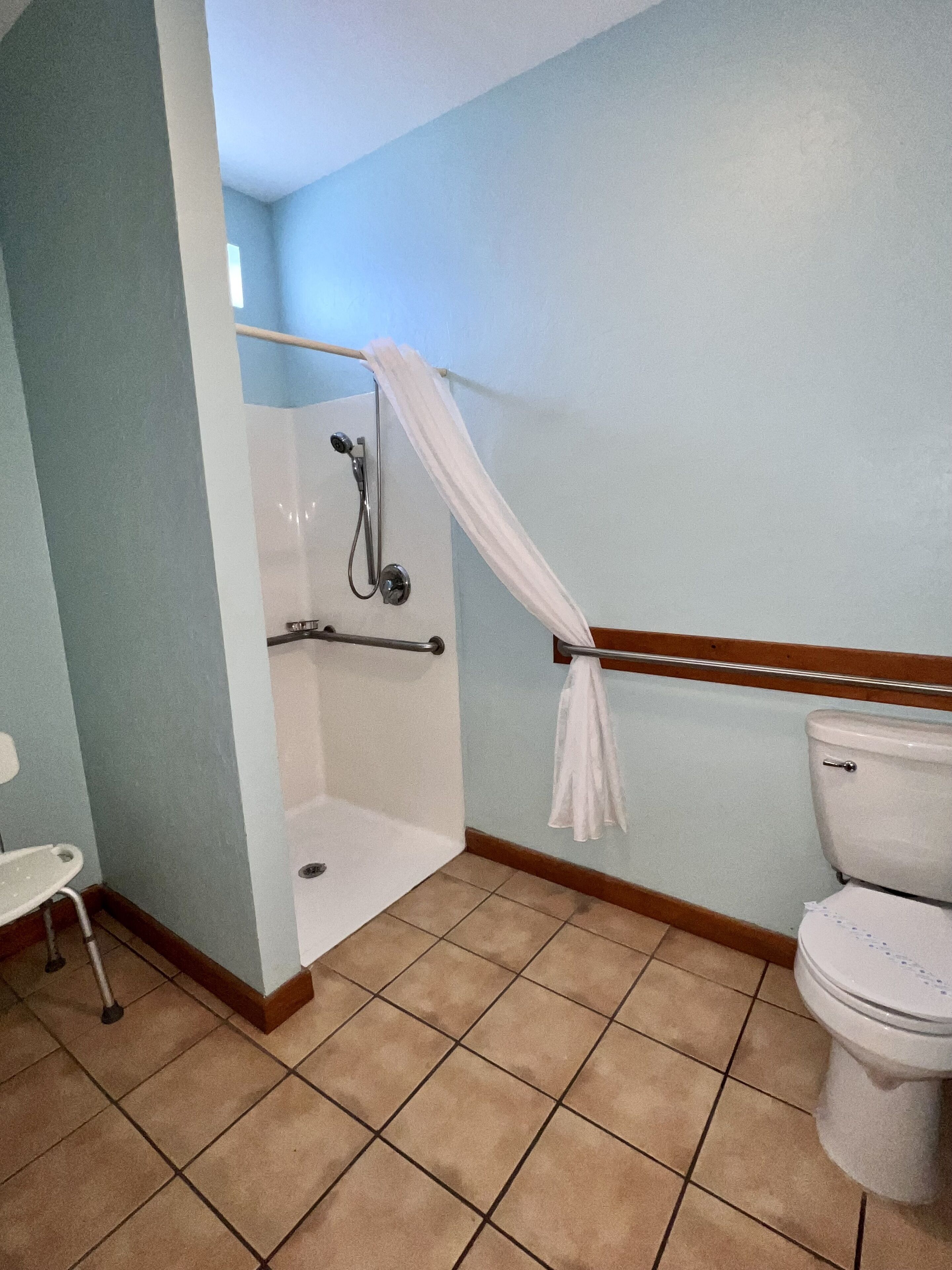 A bathroom with a shower, toilet, and a small chair.
