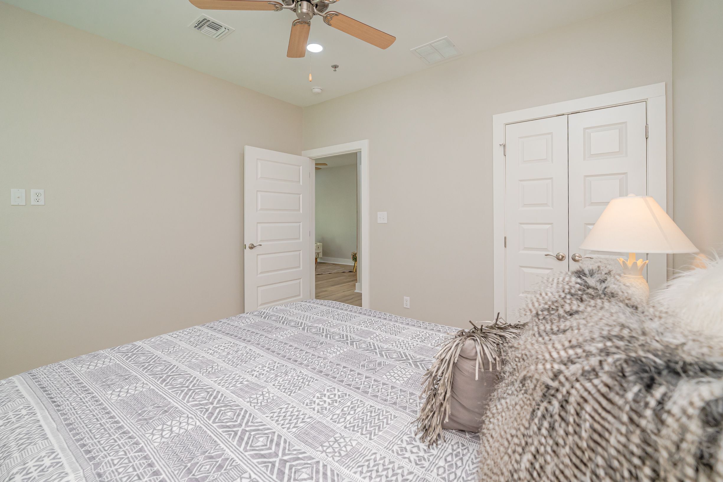 A bedroom with a patterned bedspread, a ceiling fan, and two white doors.