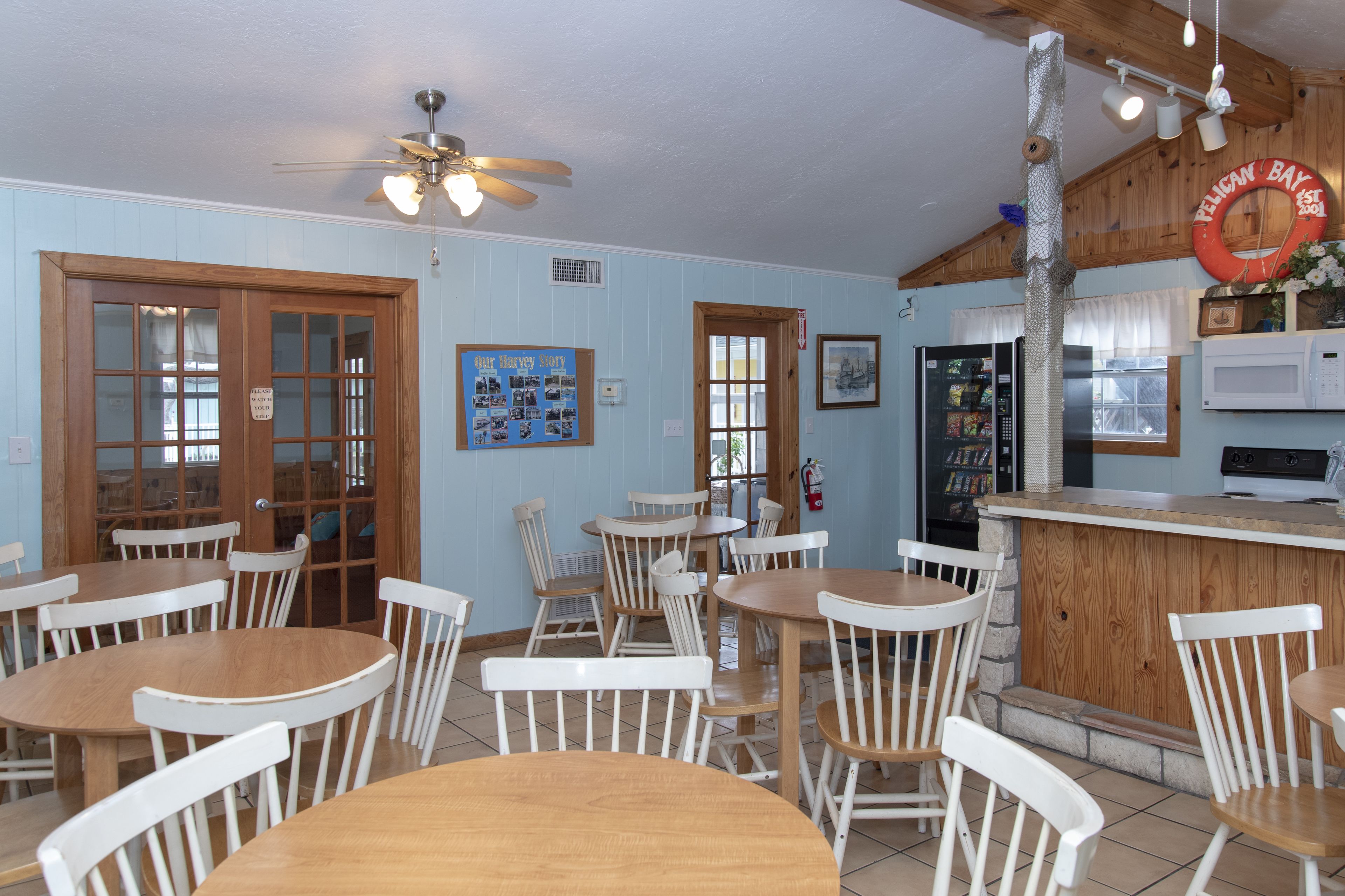 A dining area with wooden tables and white chairs, a kitchen area with a microwave, and a ceiling fan.