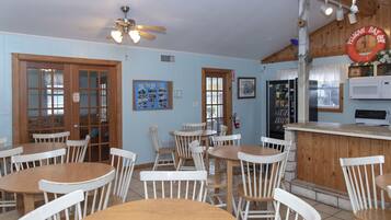 A dining area with wooden tables and white chairs, a kitchen area with a microwave, and a ceiling fan.