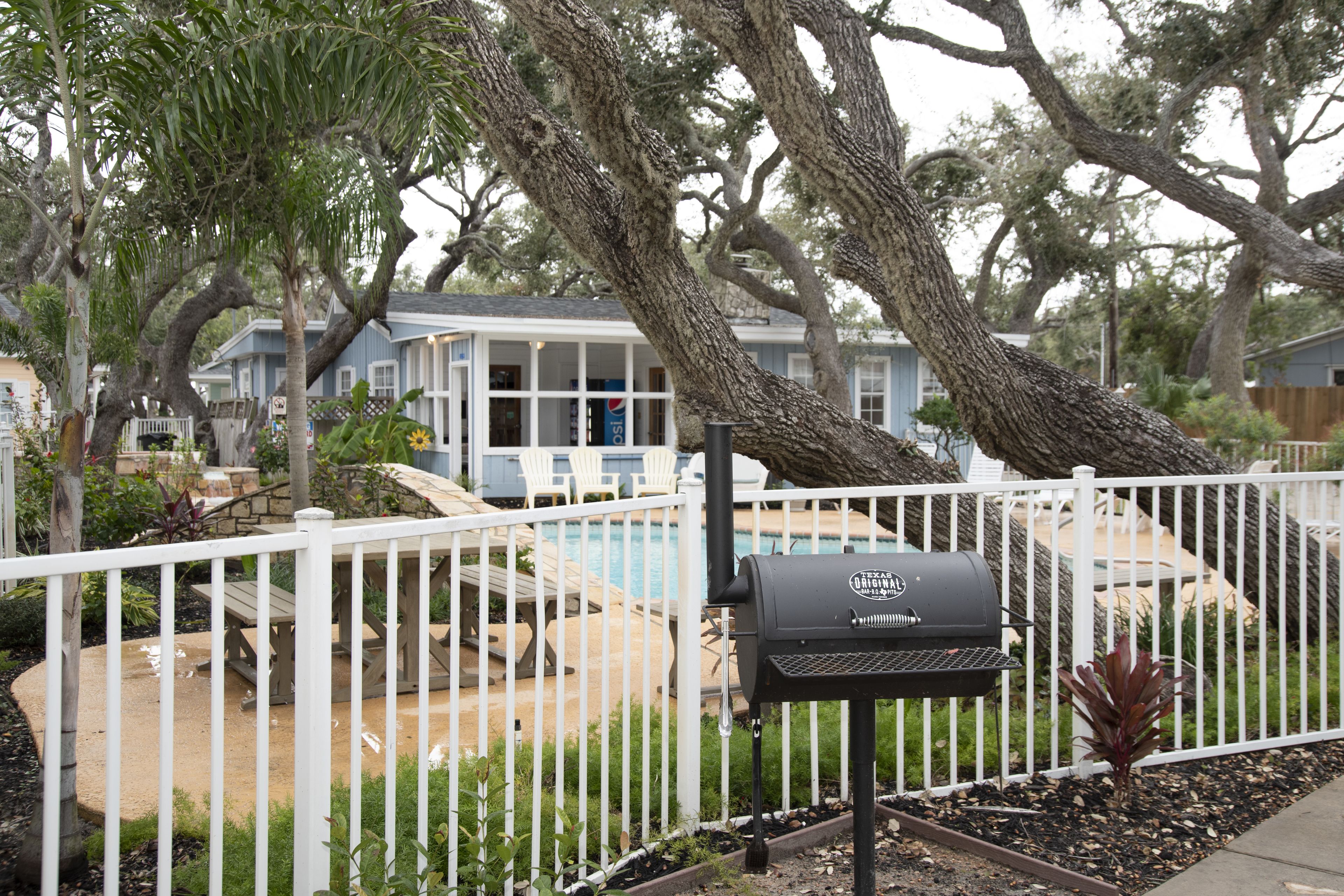 A backyard with a barbecue grill, a pool, and a white fence.