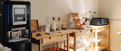 Una cocina con cafetera, microondas y lavabo. Hay cuadros en la pared y una mesa de madera con fruta y vajilla.