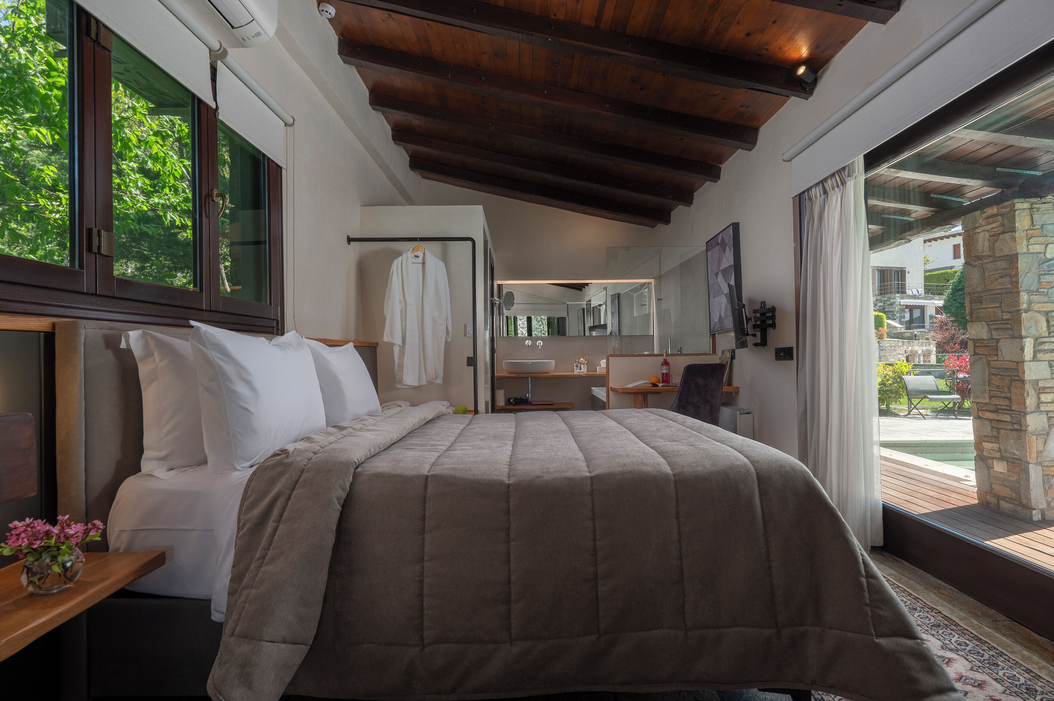 A bedroom with a large bed, a nightstand, a mirror, and a view of the outdoors.