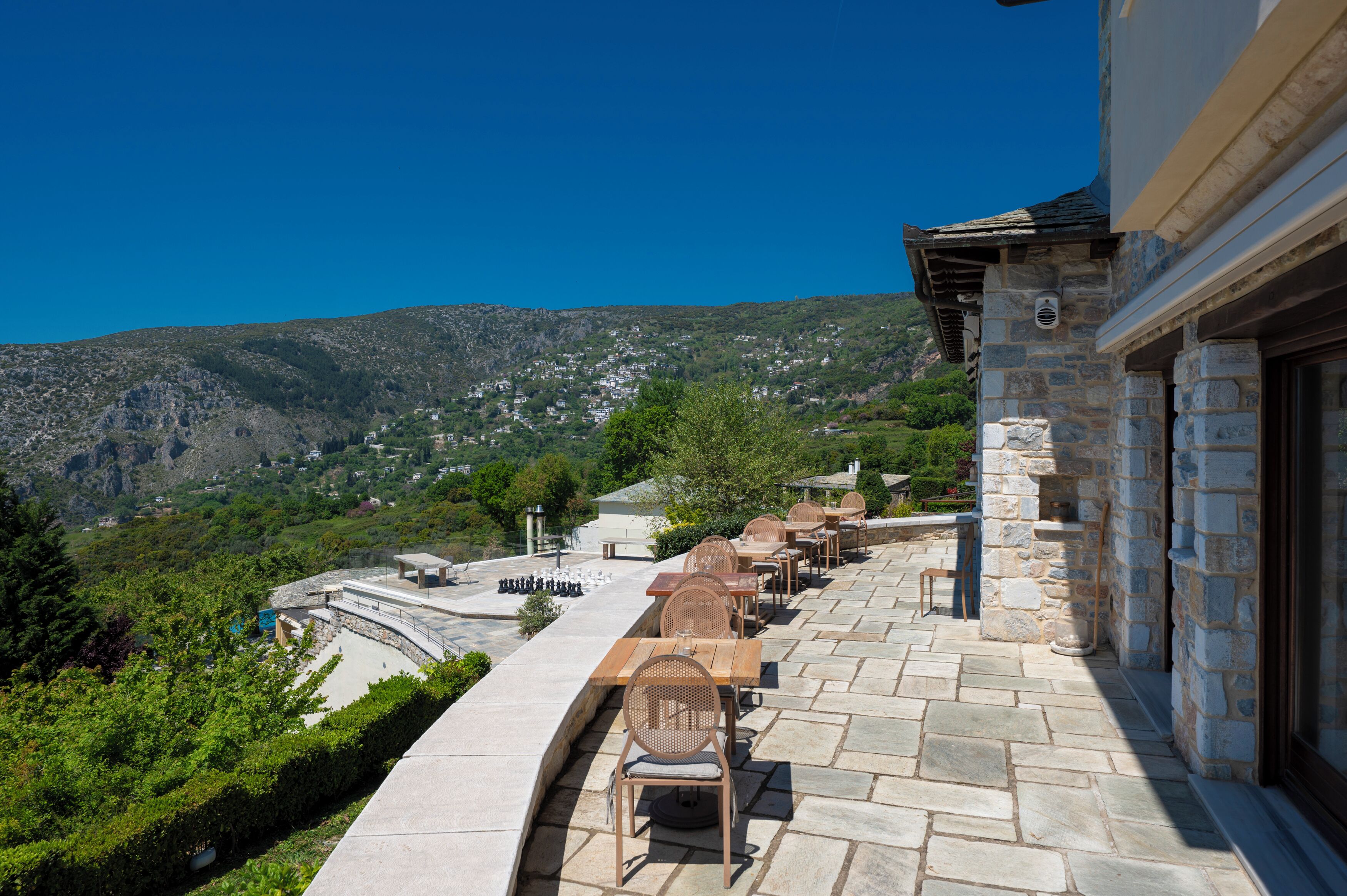 A terrace with stone flooring, outdoor seating, and a view of a mountainous landscape.