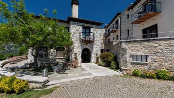 A stone building with a central entrance, outdoor seating, and a tree in the courtyard.