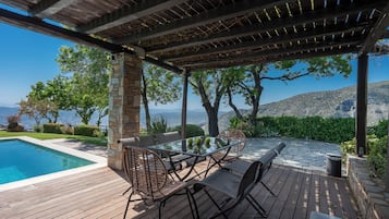 A poolside area with a pergola, outdoor furniture, and a view of the sea.