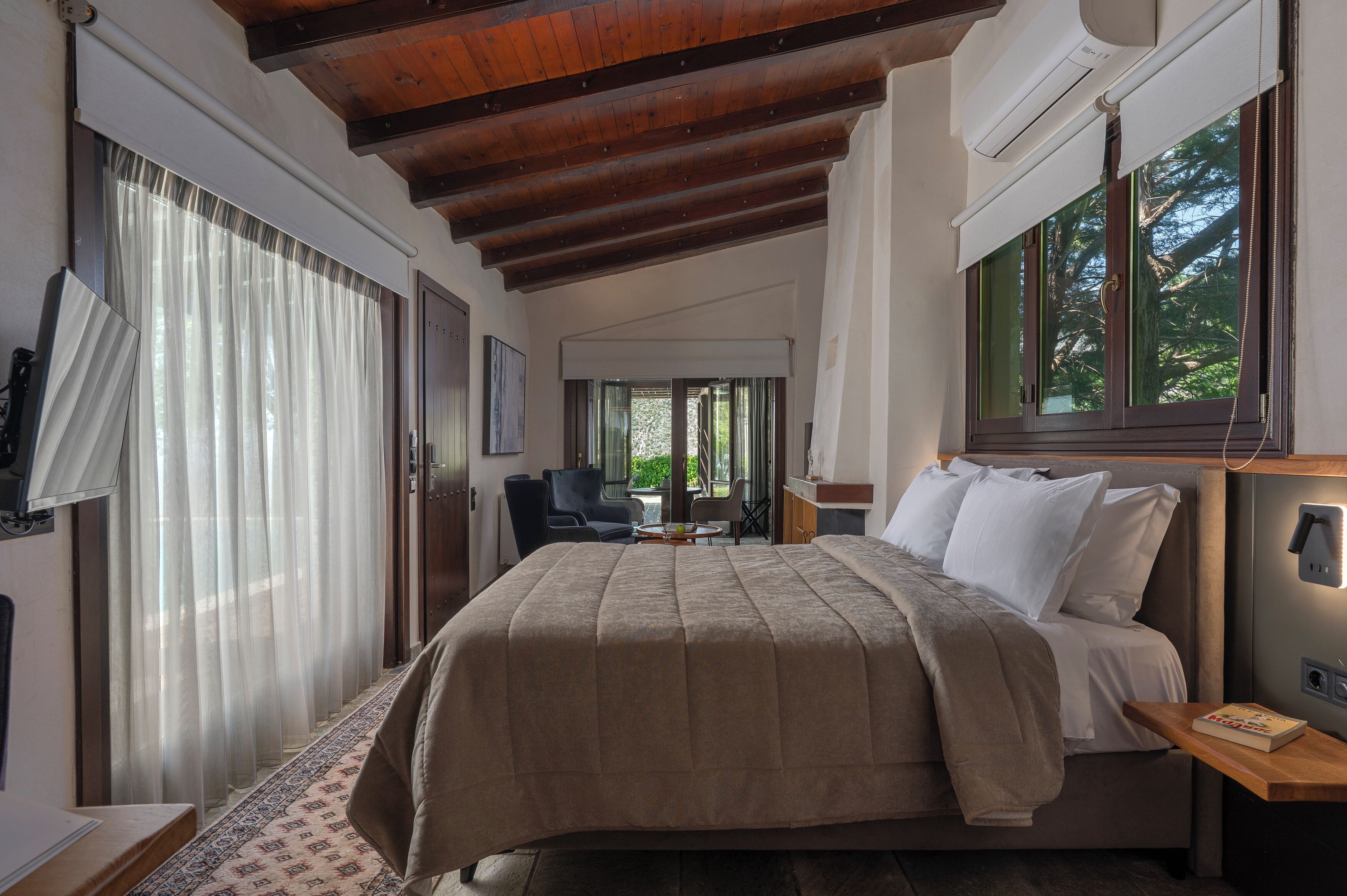 A bedroom with a bed, bedside table, and a window with a view of trees.