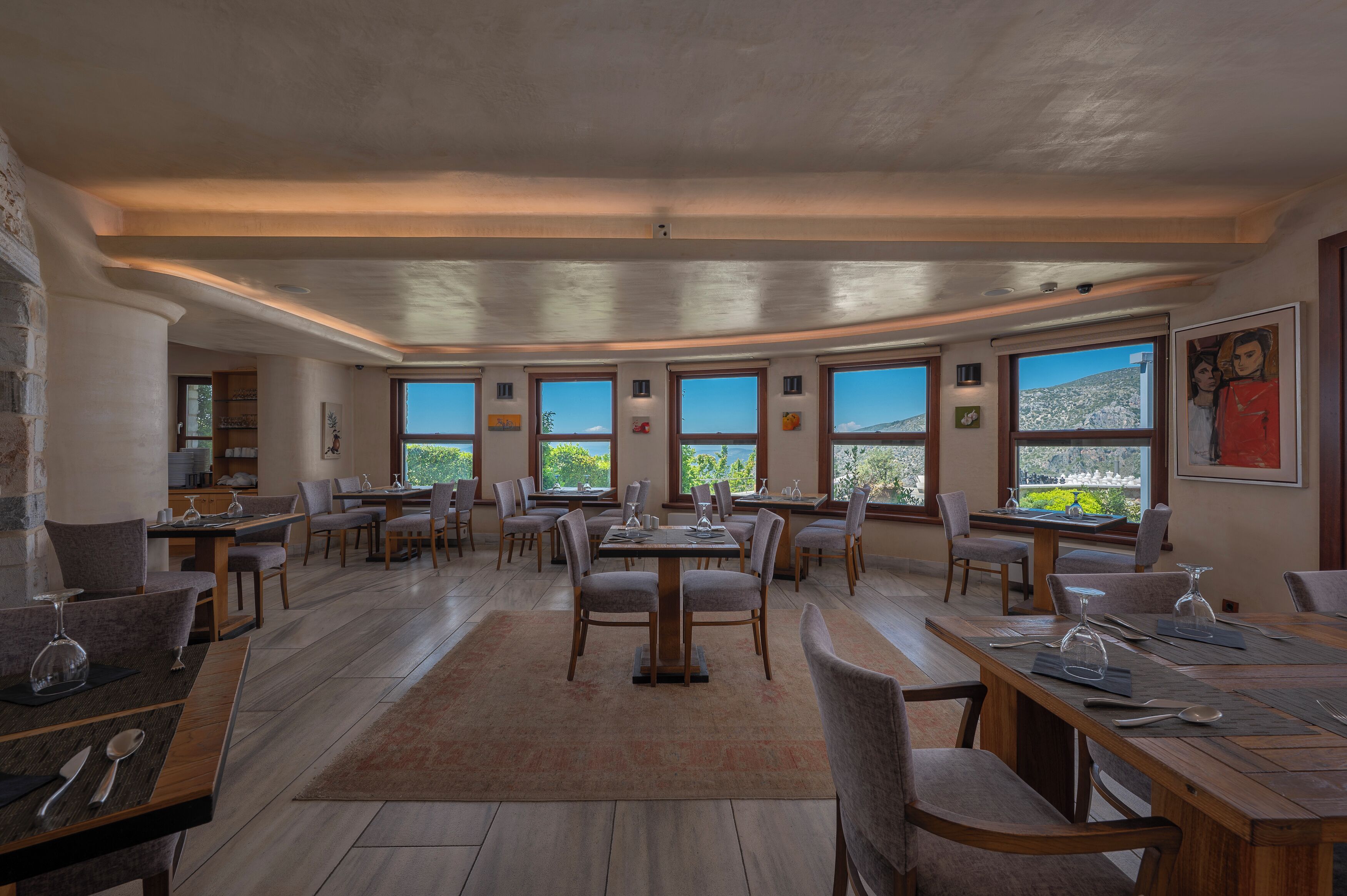Un amplio comedor con varias mesas y sillas, ventanas grandes que ofrecen vistas al exterior, y un diseño arquitectónico moderno con techos expuestos y luz natural.