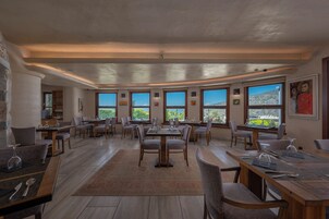 A spacious dining area with multiple tables and chairs, large windows offering views of the outdoors, and a modern architectural design with exposed ceilings and natural light.
