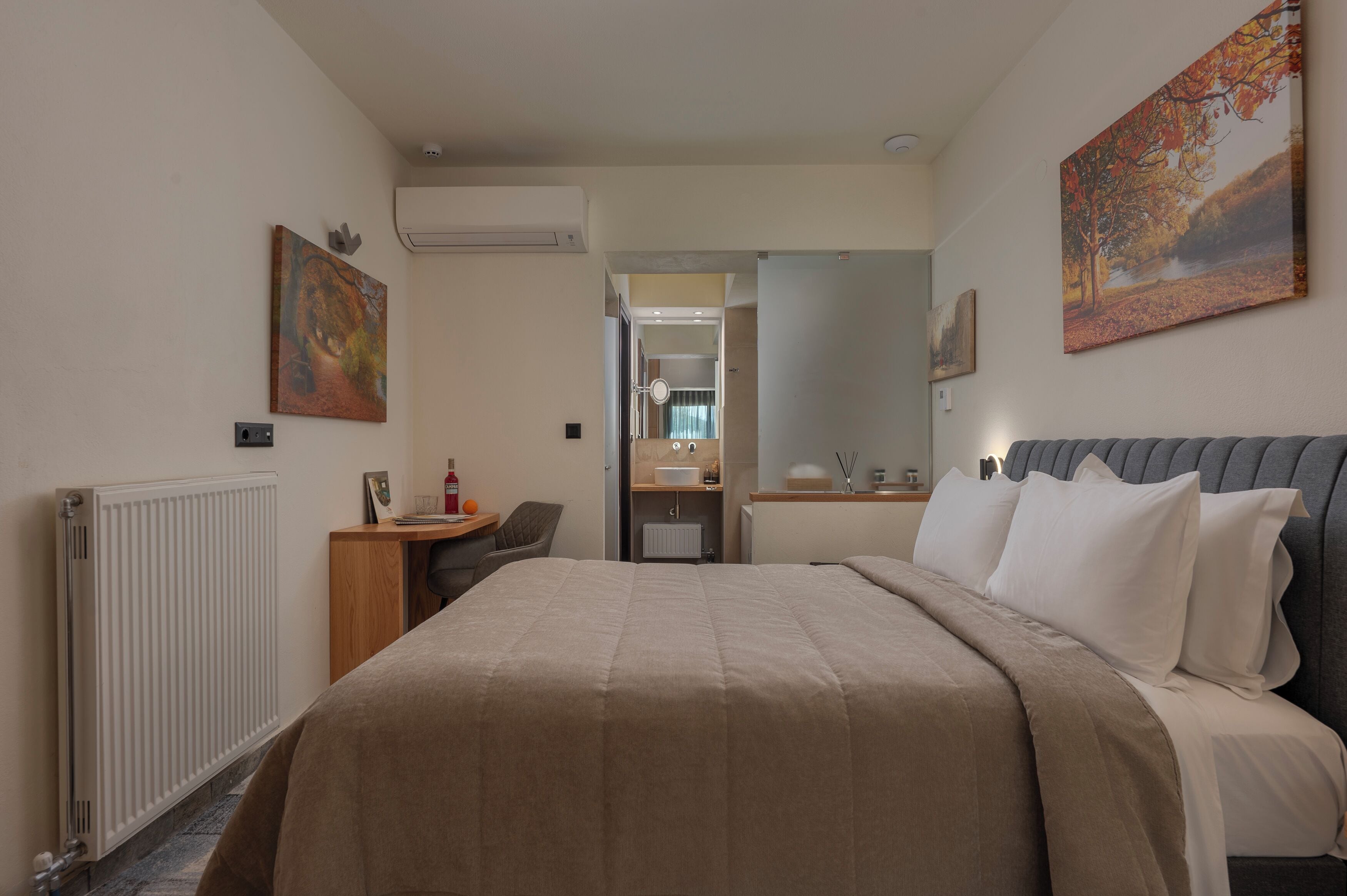 A hotel room with a bed, a desk, a chair, a mirror, and a bathroom visible through an open door.