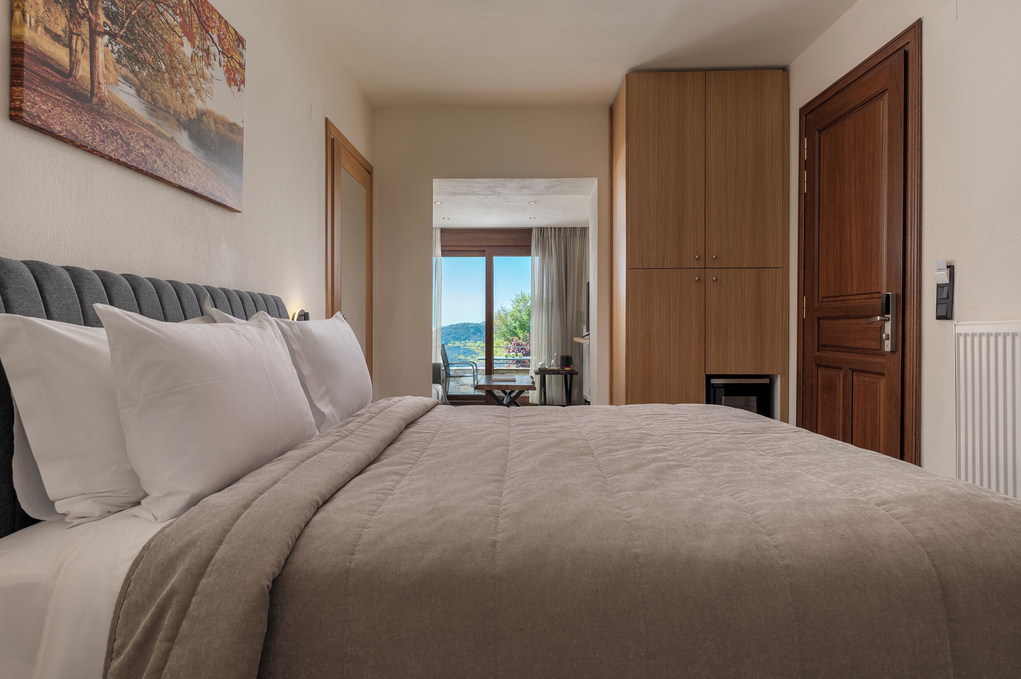 Habitación de hotel con una cama grande, vistas al exterior, muebles de madera y un cuadro en la pared.