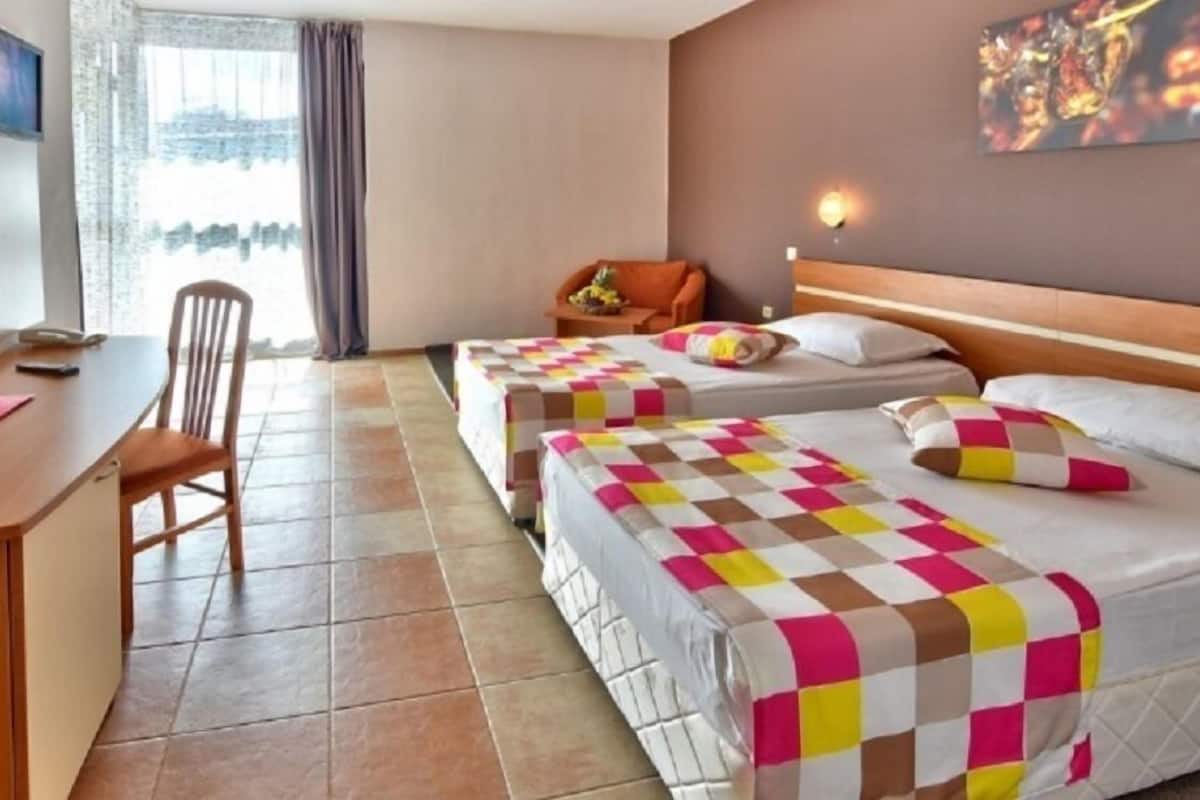 Quarto de hotel com duas camas, uma escrivaninha, uma cadeira e uma televisão.