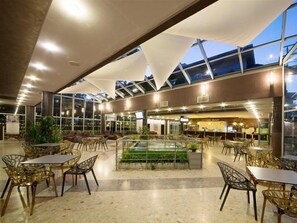 An indoor dining area with tables and chairs, a central water feature, and a glass ceiling. - Mimosa Sunshine Hotel COOEE - All Inclusive (Golden Sands)