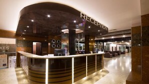 A reception area with a curved counter, a sign above it reading "RECEPTION", and a restaurant visible in the background. - Mimosa Sunshine Hotel COOEE - All Inclusive (Golden Sands)