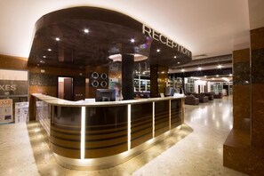 A reception area with a curved counter, a sign above it, and a restaurant in the background. - Mimosa Sunshine Hotel COOEE - All Inclusive (Golden Sands)