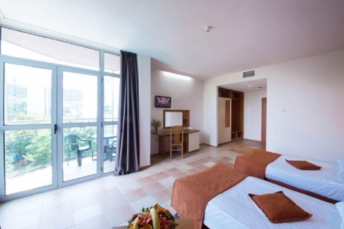Quarto de hotel com duas camas, uma mesa, televisão e varanda com vista.